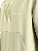 Buzo con capucha color crema, de felpa de algodón regenerativo. Tiene cordones ajustables, bolsillo tipo canguro y logo de Calvin Klein Jeans estampado en el pecho.