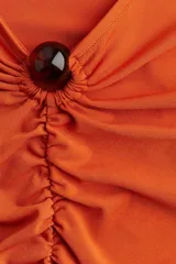 Vestido mini color naranja, entallado, de punto elástico con leve brillo, manga larga, escote en V, cuenta decorativa en el centro del busto y costura fruncida adelante para un efecto drapeado.