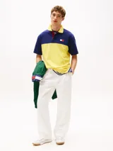 Chomba Tommy Hilfiger de corte amplio, con diseño color block en azul y amarillo, cuello clásico, cartera de tres botones, logo bordado en el pecho y logo oversize en la espalda.