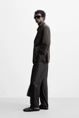 Pantalón de vestir negro de corte recto, confeccionado en tejido de algodón con acabado ligeramente encerado. Cuenta con bolsillos laterales y traseros de vivo. El cierre frontal es con cremallera y gancho metálico oculto.