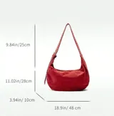 Bolso marrón de gamuza con forma de media luna y tachas plateadas. Tiene correa de hombro ajustable con hebilla metálica y cierre superior con cremallera.