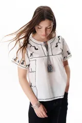 Blusa negra con bordados blancos de animales y motivos geométricos. Tiene cuello redondo con lazo y mangas cortas.