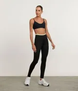 Conjunto deportivo de dos piezas, compuesto por un top deportivo de tirantes finos y un pantalón legging ajustado. Ambas prendas son de color gris oscuro, con el detalle de una banda elástica de color rosado en la cintura del legging.