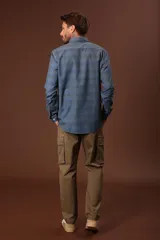 Camisa celeste con rayas horizontales en tonos beige y gris, de corte clásico, manga larga y cuello abotonado.