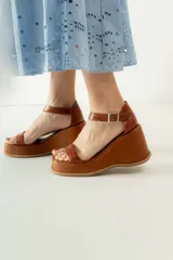Sandalias de cuero color marrón con plataforma y taco de cuña. Tiras anchas con textura tipo cocodrilo y hebilla metálica plateada.