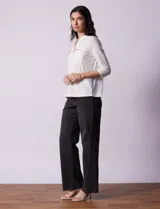 Blusa blanca de poliéster y elastano, con cuello a la base, escote en V y mangas tres cuartos. Presenta dos bolsillos frontales con cierre metálico dorado.
