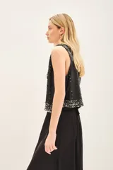 Chaleco negro con lentejuelas y apliques plateados, escote en V y cierre frontal con gancho oculto.