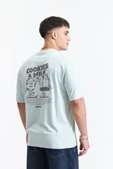 Remera azul de manga corta con corte oversize y cuello redondo. Estampado en la espalda con la frase "Cookies & Milk" y dibujos de una galleta y un cartón de leche.
