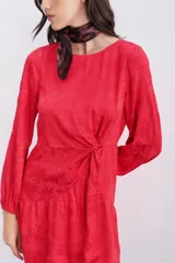 Vestido corto rojo con estampado floral, escote redondo, mangas largas con elástico en los puños, detalle de nudo drapeado en la cintura y escote en V pronunciado en la espalda.