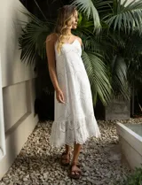 Vestido blanco de broderie con escote en V, corte bajo el busto y breteles finos cruzados en la espalda. Tiene forro interno a tono y largo midi.