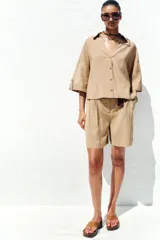 Camisa color beige de cuello solapa con escote pico y manga corta ancha acabada en vuelta con trabilla y botón. Cierre frontal con botones.