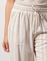 Pantalón de lino a rayas verticales color beige y blanco, con pretina ancha elastizada, lazo de ajuste y bolsillos inclinados.