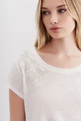 Remera de mangas cortas color crudo, confeccionada en lino y viscosa. Presenta bordados a tono con apliques de lentejuelas, canutillos y mostacillas en la parte superior.