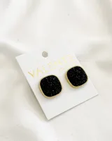 Par de aros tipo botón cuadrados, con base dorada y superficie cubierta de pequeñas piedras negras brillantes.