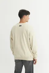 Buzo de felpa color beige con arte bordado en el pecho y estampado en la manga, de calce oversize.
