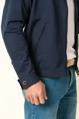 Campera color beige con cierre frontal, cuello camisero, bolsillos laterales y elástico en la cintura. Detalle de bolsillo en la manga izquierda.