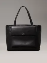 Cartera tote Calvin Klein color negro, confeccionada en piel sintética, con doble asa de hombro, cierre superior con cremallera, bolsillo externo con cierre giratorio y logo CK plateado.