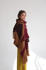Ruana de lana con diseño abstracto en tonos beige, marrón y blanco. Presenta flecos en el borde inferior y capucha.