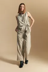 Pantalón de vestir de tiro alto, color beige claro con finas rayas verticales oscuras. Es de corte ancho y largo, con un lazo de tela a juego anudado en la cintura. Se combina con un top sin mangas del mismo tejido y color.