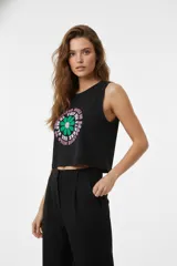 Musculosa negra de algodón con cuello a la base y corte holgado. Presenta un estampado gráfico frontal con una flor verde y texto circular en tonos rosados.
