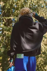 Buzo negro con capucha, cierre frontal, calce relajado y ligeramente holgado, con costuras definidas, hombros caídos y mangas levemente amplias.