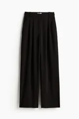 Pantalón de vestir negro de corte ancho y tiro alto, con cintura elástica oculta y cierre. Presenta bolsillos al bies, bolsillos decorativos insertados atrás y pliegues delanteros.