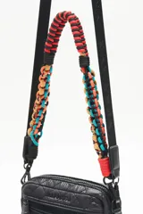 Bandolera negra de nylon matelassé con correa larga regulable y correa corta desmontable de cordones trenzados multicolores. Tiene cierre superior, bolsillo frontal con cierre, bolsillo trasero y dos bolsillos internos.