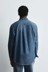 Camisa relaxed fit confeccionada en denim de algodón con cuello solapa, manga larga con puño abotonado, efecto lavado medio y cierre frontal con botones.