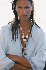 Collar con cadena dorada de eslabones y cuentas de resina en tonos beige y blanco. Dije central con forma de flor esmaltada y colgante con piedras de diferentes tamaños y colores.