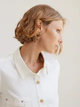Camisa de corte clásico con detalles bordados en color beige, botones de madera y bolsillo frontal.