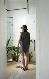 Vestido corto de jean gris con botones frontales, sin mangas, con cuello camisero y bolsillos en el pecho.