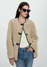 Chaqueta de tejido efecto borreguito color beige, con cuello redondo, cierre de botones de trenca y dos bolsillos delanteros.