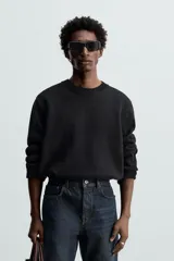 Jersey negro de corte boxy fit, tejido en hilatura con mezcla de algodón y 13% de cashmere. Tiene cuello redondo, manga larga y acabados en rib.