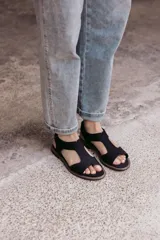 Sandalia plana de color tostado confeccionada en una combinación de neopreno y cuero. Posee un diseño de tira ancha con aberturas sobre el empeine, plantilla acolchada y suela de goma con costuras a la vista.