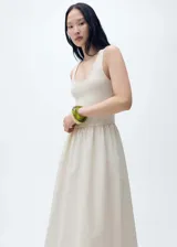 Vestido midi color crema, con tirantes anchos y escote redondo. Presenta panel fruncido en la cintura y falda evasé.