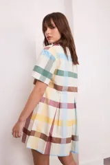 Vestido corto de algodón a cuadros color crema, verde y borgoña, con cuello redondo y mangas cortas. Presenta tablas en la parte delantera y trasera.