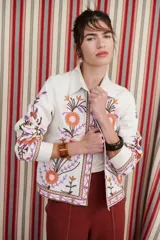 Chaqueta color crudo con bordados de flores azules y naranjas.