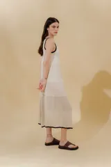 Vestido midi color crema, tejido de punto con bloques de diferentes texturas, escote redondo y sisas con terminación ondulada.