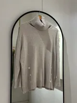 Sweater oversize color beige con cuello alto drapeado y mangas largas caídas.