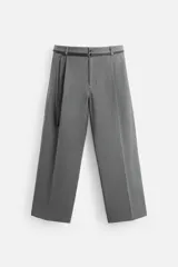 Pantalón gris de corte ancho con pliegues frontales y cinturón fino negro.