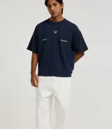 Pantalón de corte skater confeccionado en sarga de algodón color crudo, con cintura con trabillas, cordón ajustable, cierre tradicional, bolsillos y costuras contrastantes.