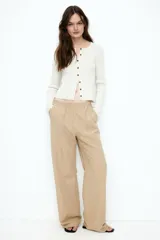 Pantalón color beige de lino con tiro alto, cintura elástica, bolsillos al bies y bolsillos traseros insertados. Piernas rectas con pliegue cosido adelante.