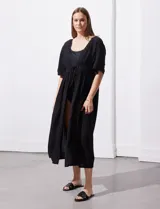 Kaftan blanco largo con mangas cortas y abertura central. Presenta apliques de puntilla en el escote, cintura y ruedo. Se ata en la cintura con un lazo.