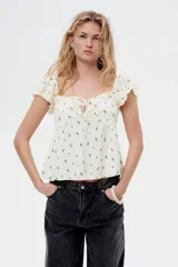 Top corto color crema con estampado floral en negro, escote corazón, manga corta circular y sección cut-out con cordón para ajustar en el busto.