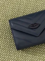 Billetera pequeña color visón, con solapa y cierre a presión. Diseño acolchado con pespuntes en forma de V y logo metálico con forma de labios.