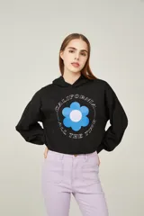 Buzo negro cropped con capucha y mangas largas abullonadas. Estampado frontal con una flor azul y texto en blanco.