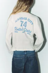 Sudadera corta color crudo de algodón, con cuello redondo, mangas largas y texto estampado en el frente que dice "IN MY YEEHAW ERA".