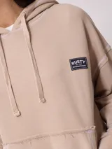 Canguro gris con capucha corta, bolsillo tipo canguro y parche con logo de la marca Rusty en el pecho. Tiene efecto lavado y costuras a la vista.