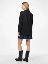 Blazer negro con cuello clásico, cierre de botones y bolsillos frontales. Tiene tachas plateadas en el frente y las mangas.
