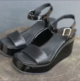Sandalias negras de charol con plataforma y taco de cuña. Tira ancha sobre los dedos y pulsera con hebilla al tobillo.